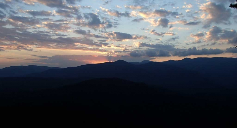 The sun is setting or rising behind a mountain range, illuminating the sky in blue, yellow and pink.